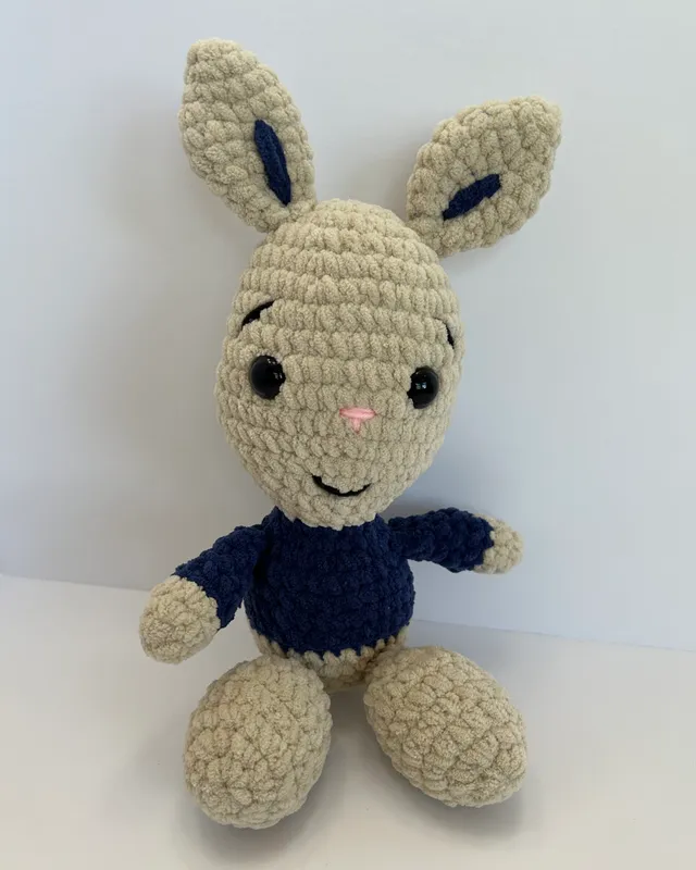 A beige crocheted bunny with long ears wearing a navy sweater.