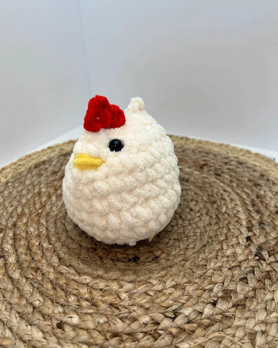 A round white crocheted chicken with a red comb and a yellow beak.