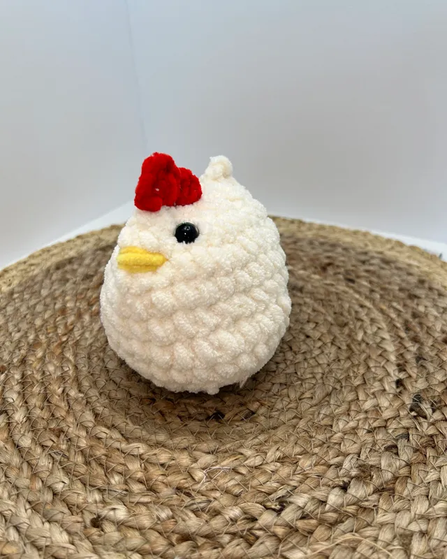 A round white crocheted chicken with a red comb and a yellow beak.