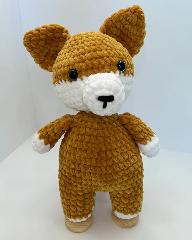 A standing crocheted fox in golden brown with a white face and white paws.