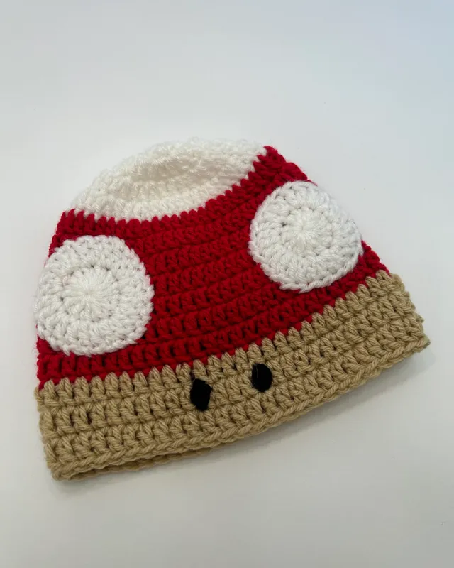 A crocheted beanie styled as a red mushroom cap with white spots.