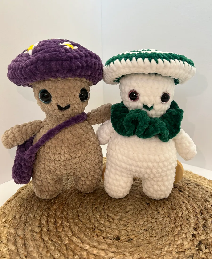 Two crocheted mushroom figures standing side by side, one with a purple cap and one with a green and white cap.