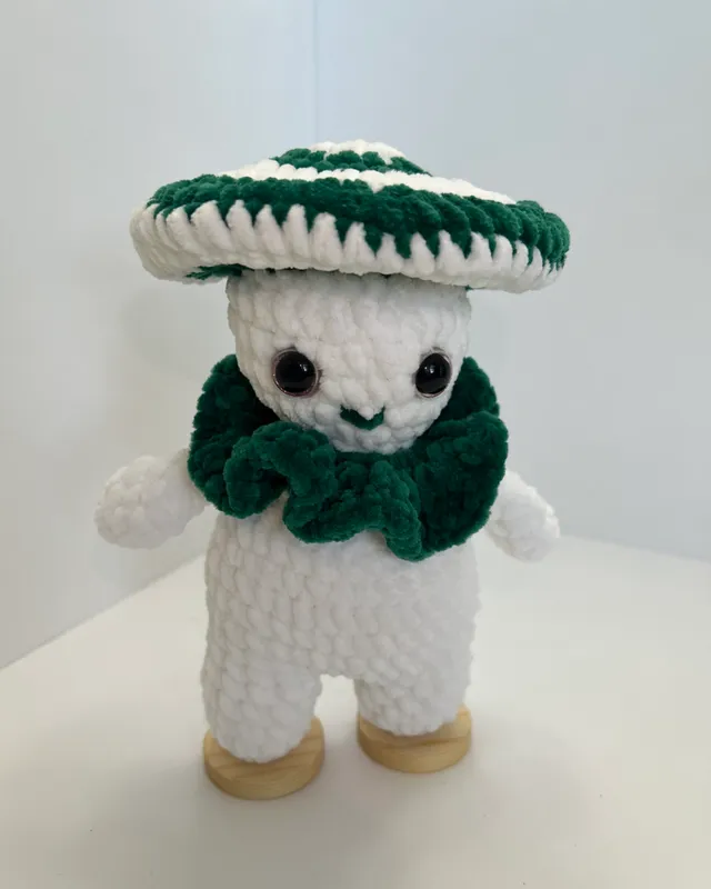 A white crocheted mushroom figure with a green and white striped cap and a green ruffled collar.