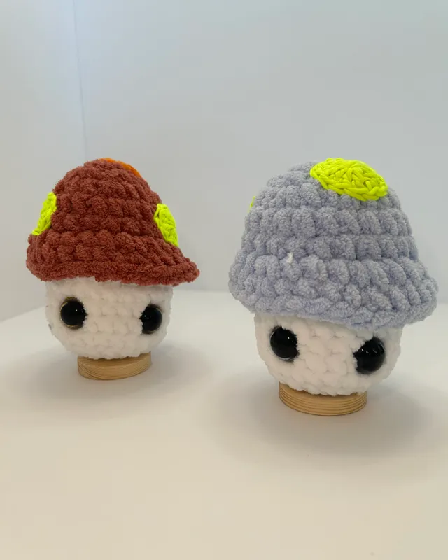 Two small crocheted mushroom toys, one with a rust cap and one with a grey cap.