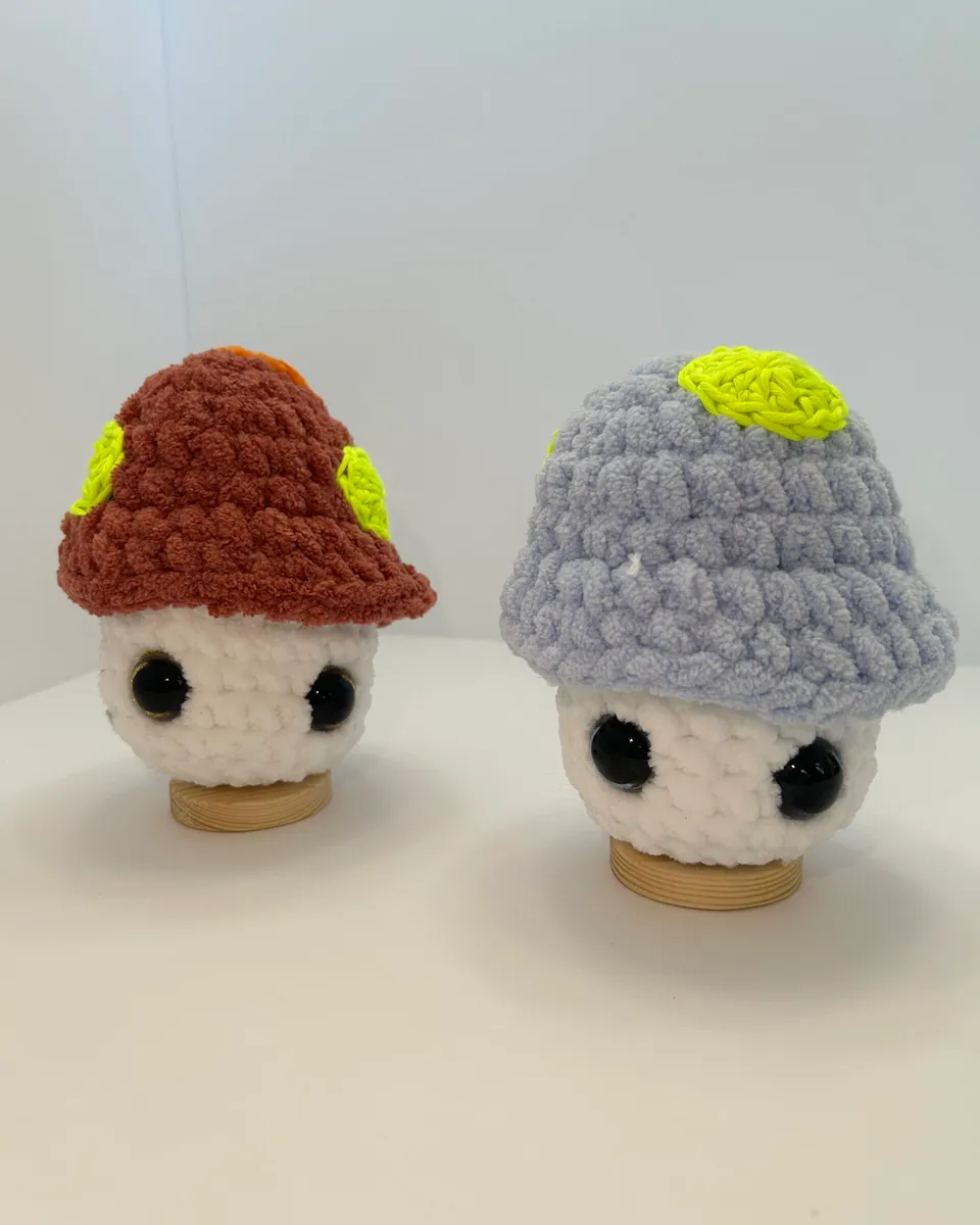 Two small crocheted mushroom toys, one with a rust cap and one with a grey cap.