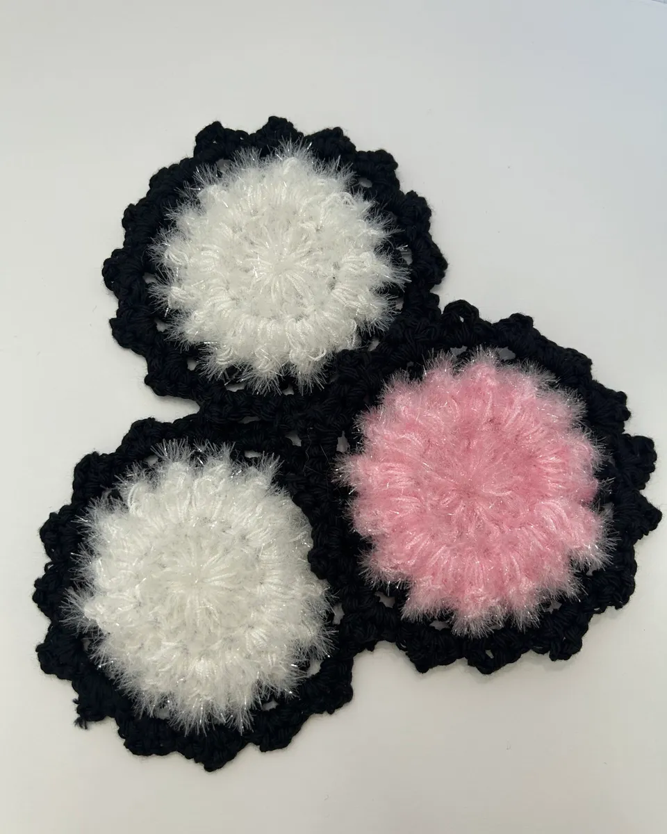 Three round crocheted scrubbies, two white and one pink, each edged in black.