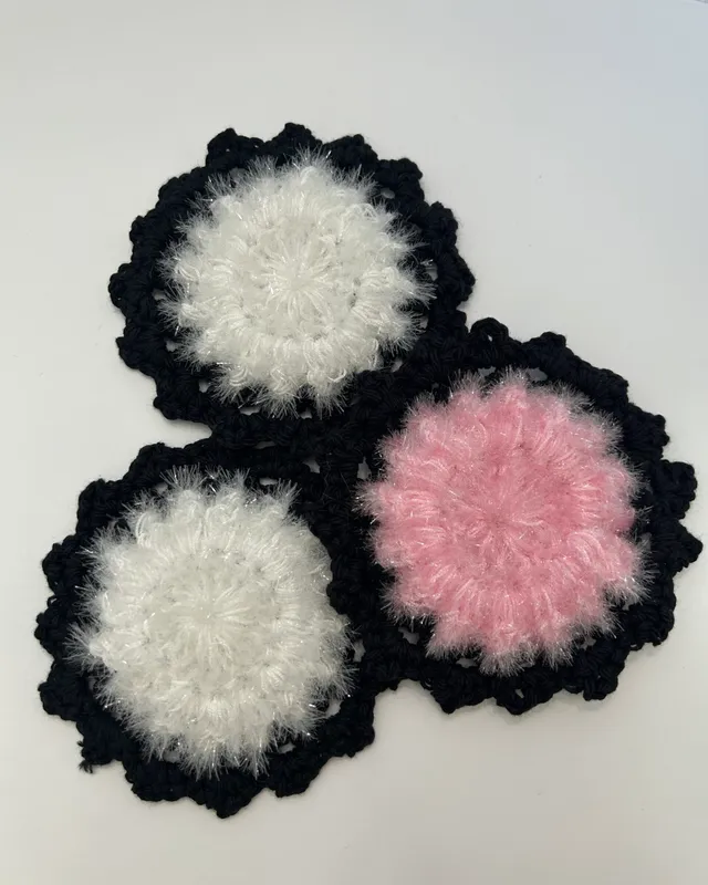 Three round crocheted scrubbies, two white and one pink, each edged in black.