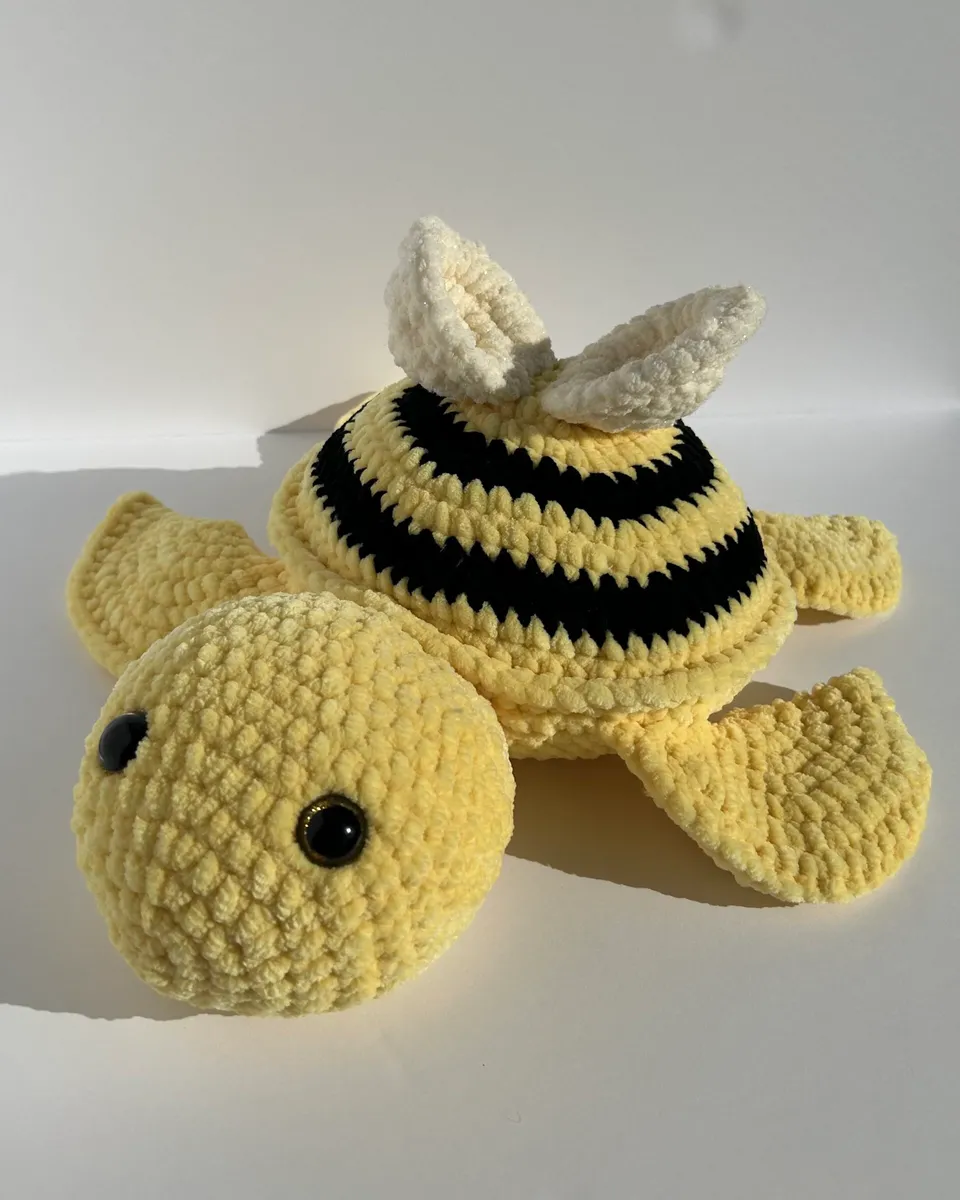 A yellow crocheted turtle with a black and yellow striped bee shell and a bow.
