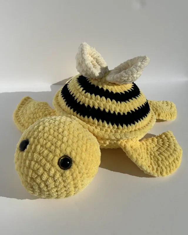 A yellow crocheted turtle with a black and yellow striped bee shell and a bow.